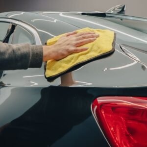 Close-up of hand polishing a shiny car with a yellow cloth indoors.