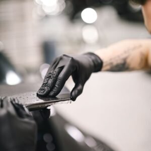 Mechanic uses black gloves for detailing a car in a garage setting.