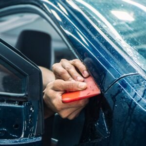 Close-up of a technician installing PPF on a car door in a workshop.